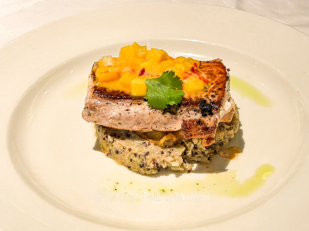 A piece of grilled fish is topped with a medley of orange and yellow fruits.