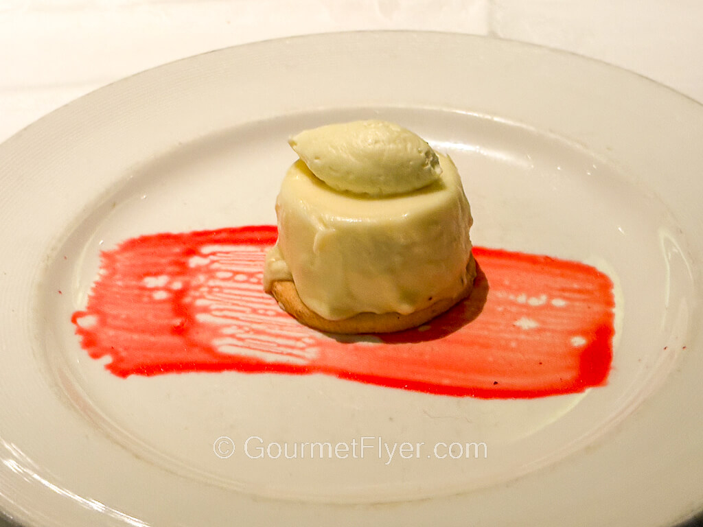 A green mousse-like dessert is presented with a brush of strawberry syrup.