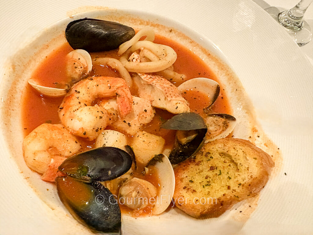 A large soup bowl contains a mix of shellfish served in a red broth.