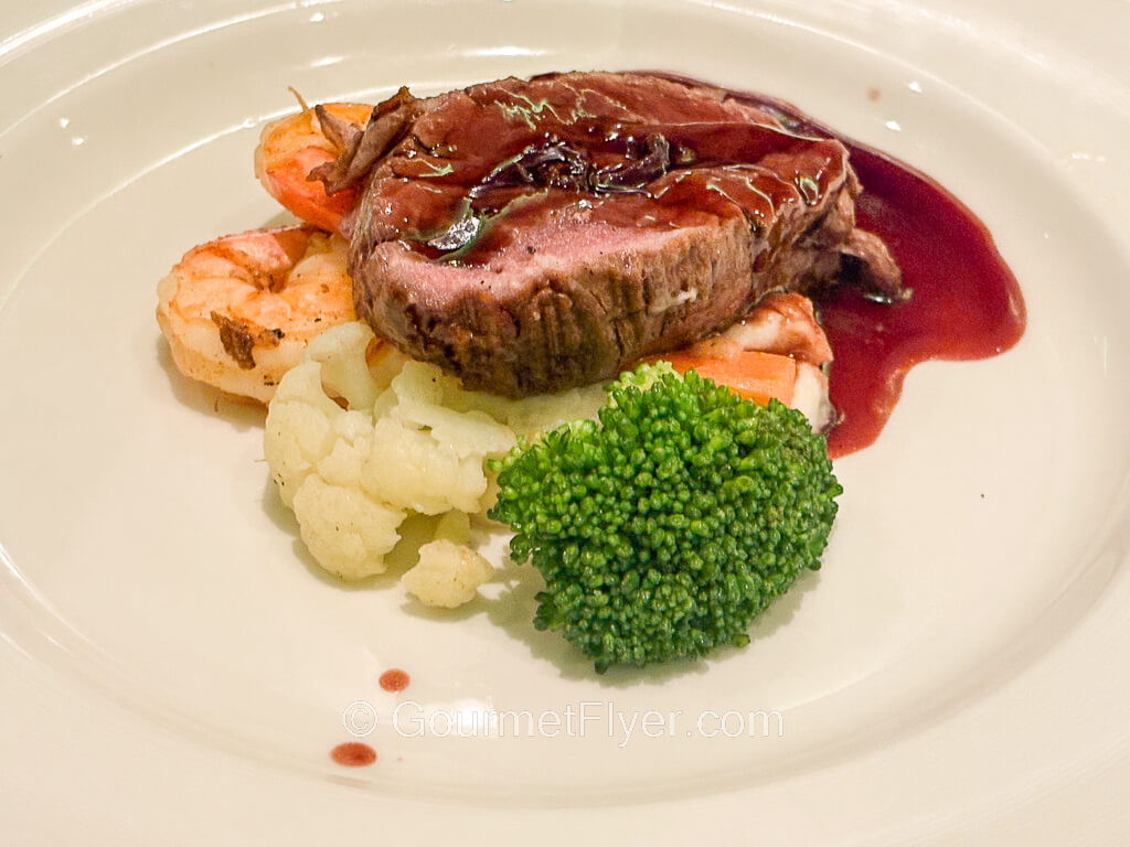 A beef filet accompanied with two shrimps are garnished with broccoli and cauliflower florets.