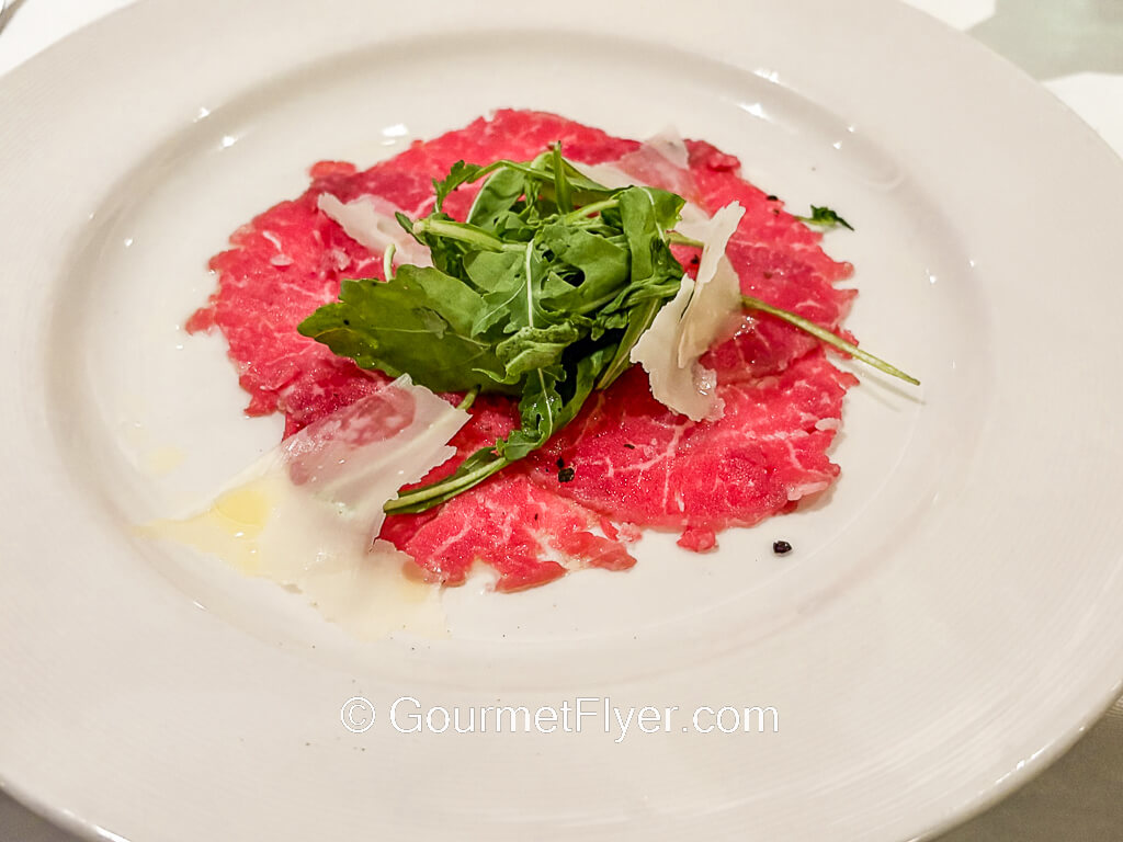 Thin slices of red meat is served on a plate and accompanied with green lettuce.