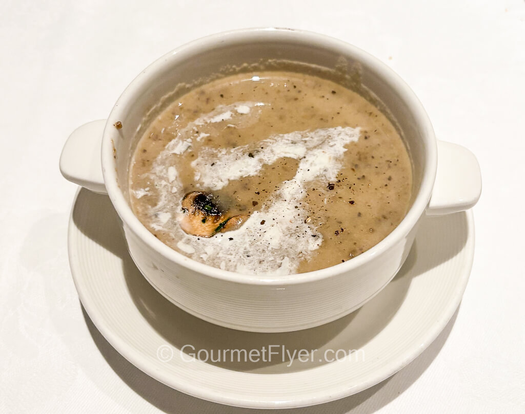 A cup of creamy soup is topped with heavy cream.