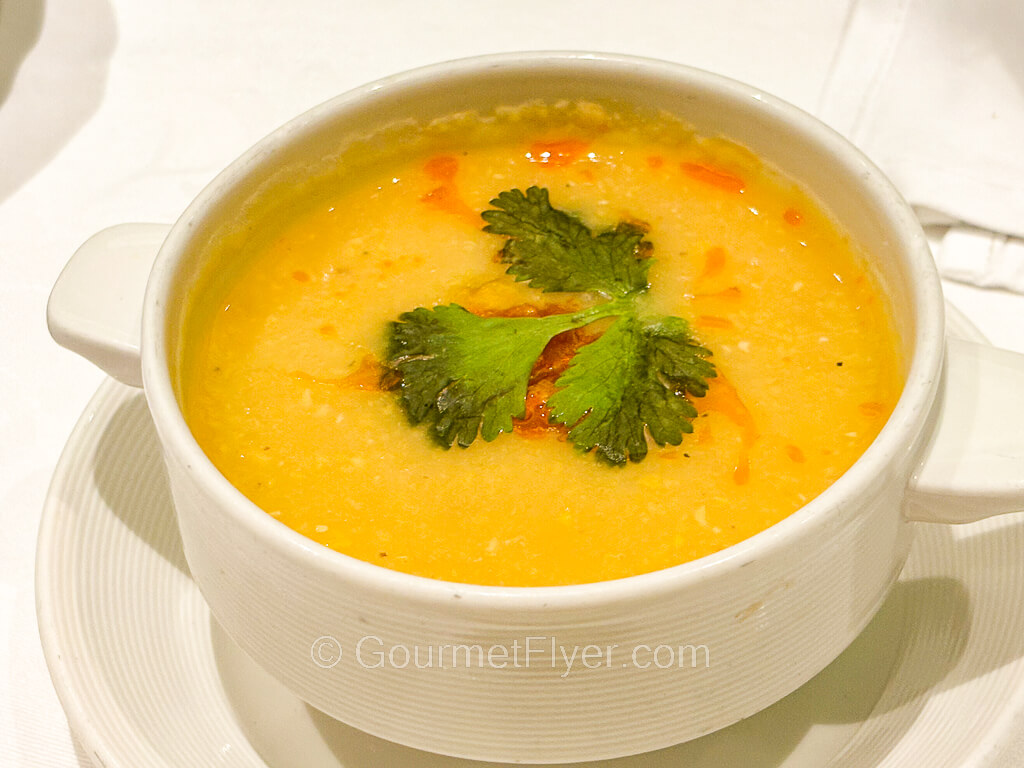 A bowl of yellowish creamy soup garnished with parsley leaves.