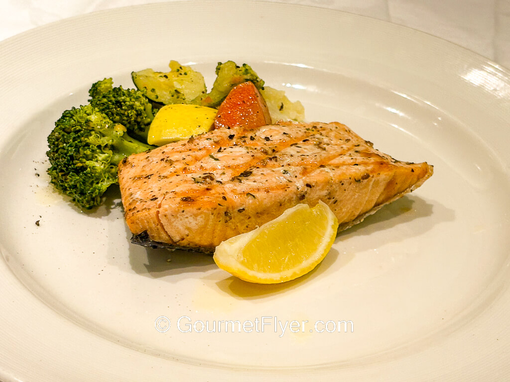 A plate of grilled fish is served with vegetables and a wedge of lemon.