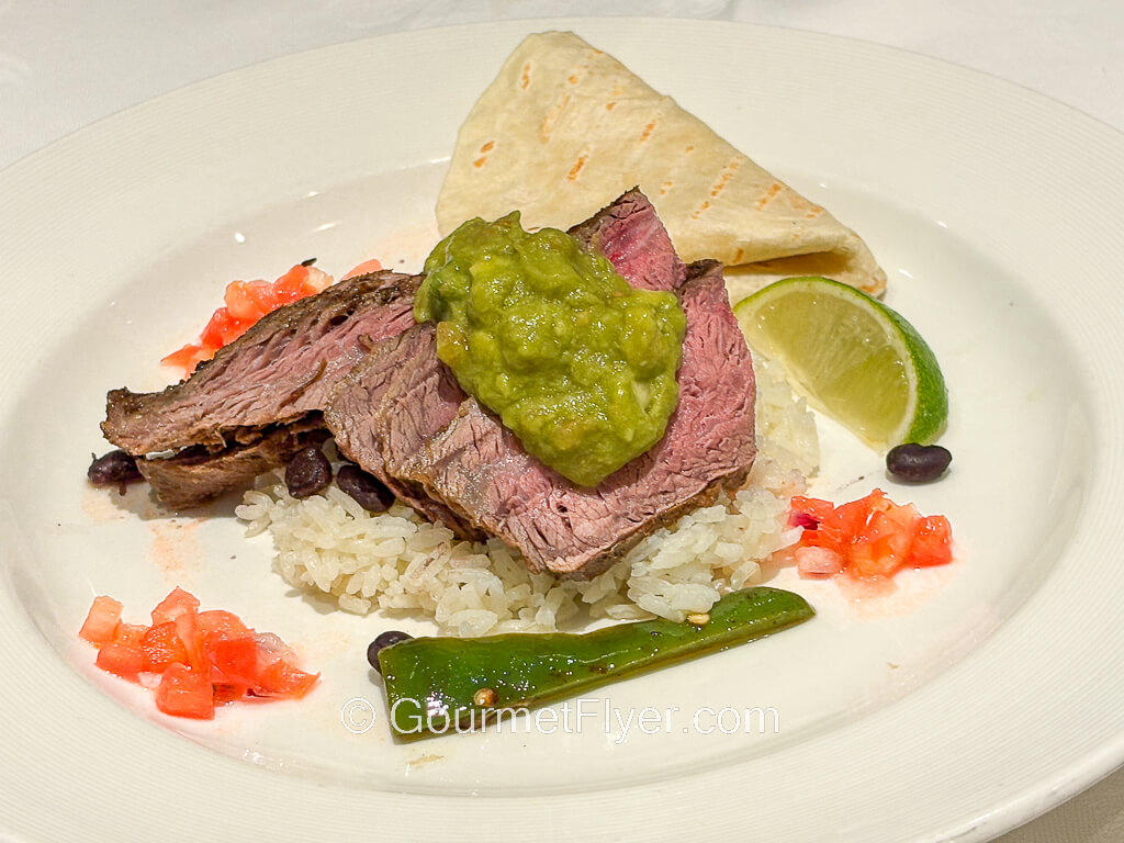 Slices of beef is served with guacamole and flour tortillas. 