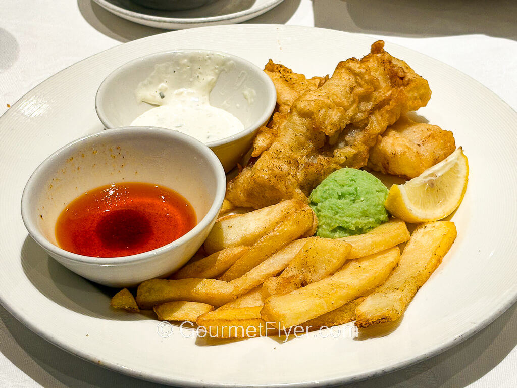 Fried fish and French fries are served with a side of tartar sauce and vinegar.