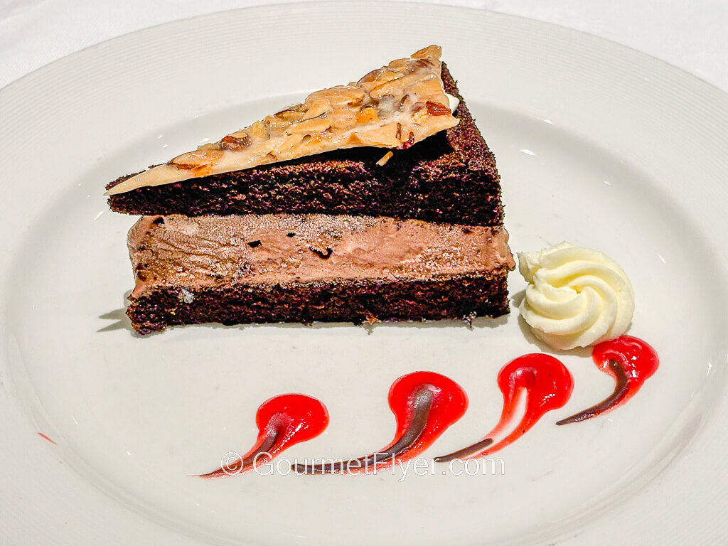 A layered chocolate cake is served on a plate and accompanied by whipped cream.