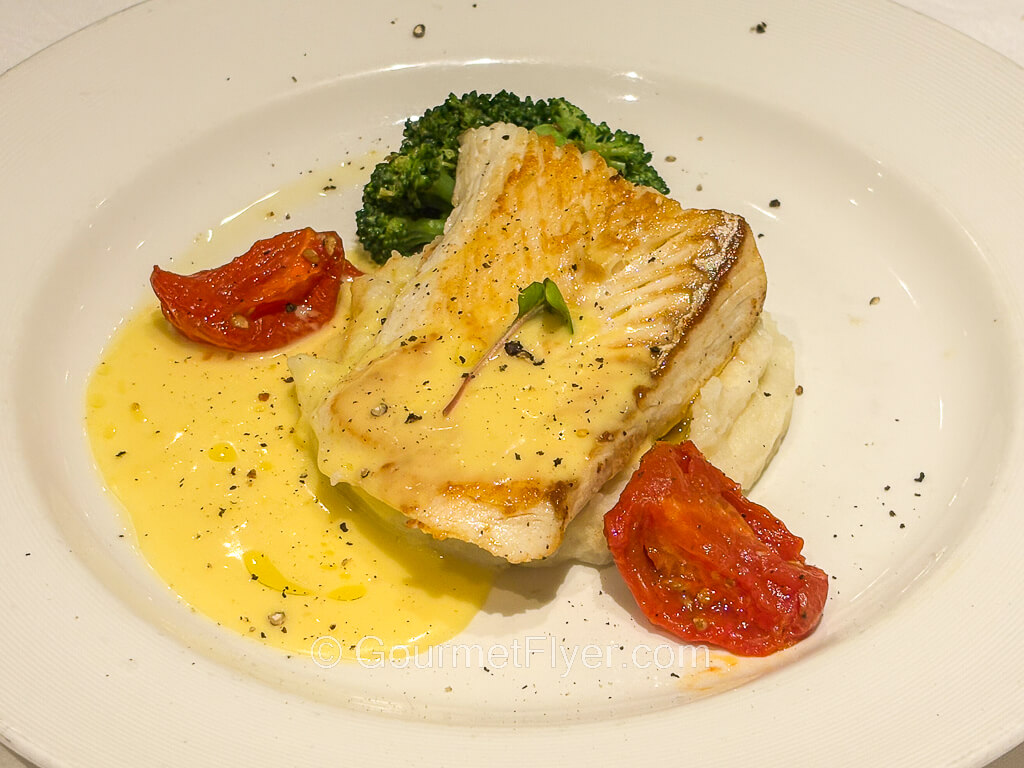 A piece of fish is plated with yellowish creamy sauce.