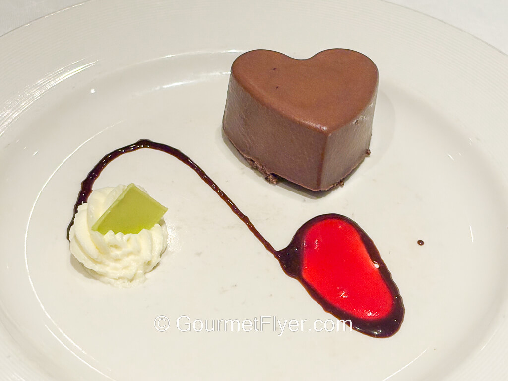 A heart shaped chocolate dessert is served with whipped cream.