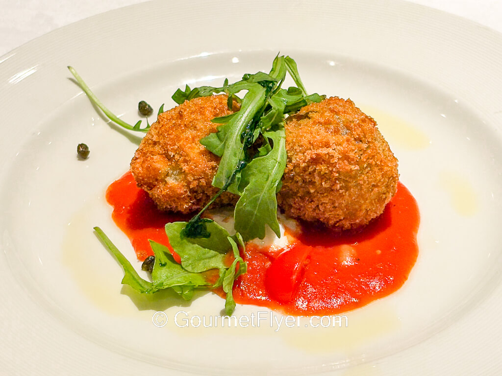 Two fried dumplings are served with a red sauce and garnished with arugula leaves.