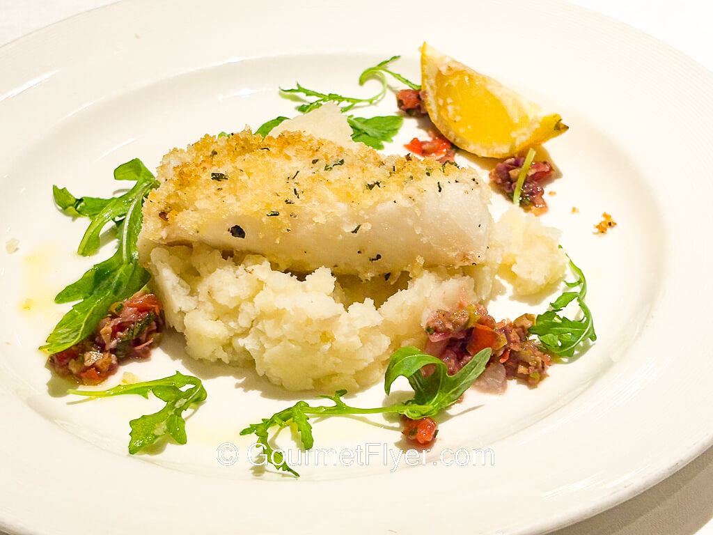 A piece of fish is garnished with greens and a wedge of lemon.