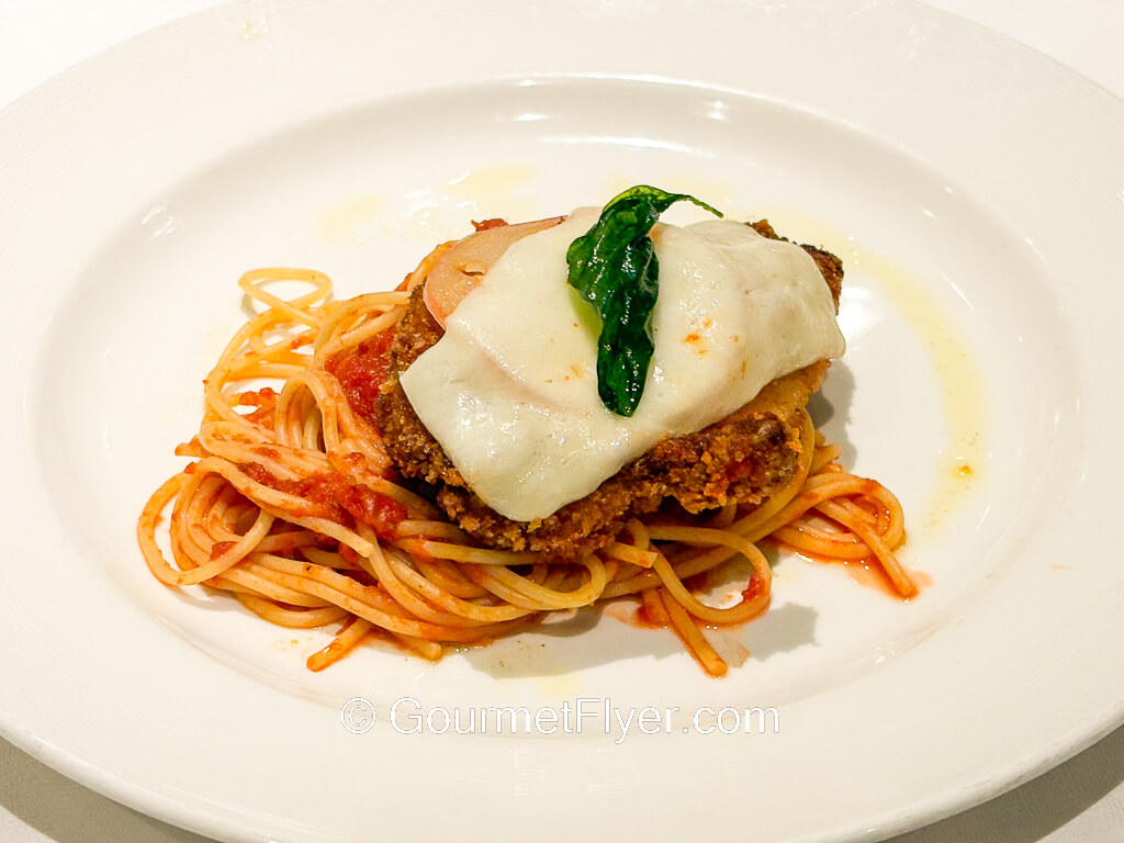 A piece of fried meat is topped with melted cheese and served over spaghetti in a red sauce.