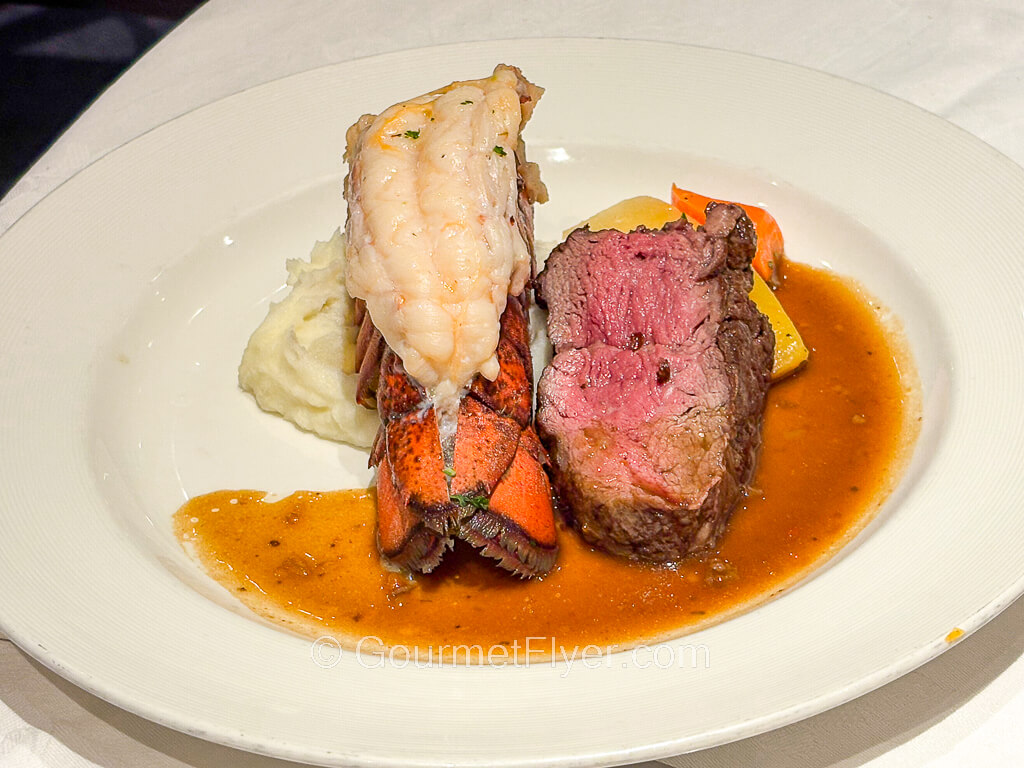 A medium rare slab of beef is paired with a lobster tail and served with brown gravy.