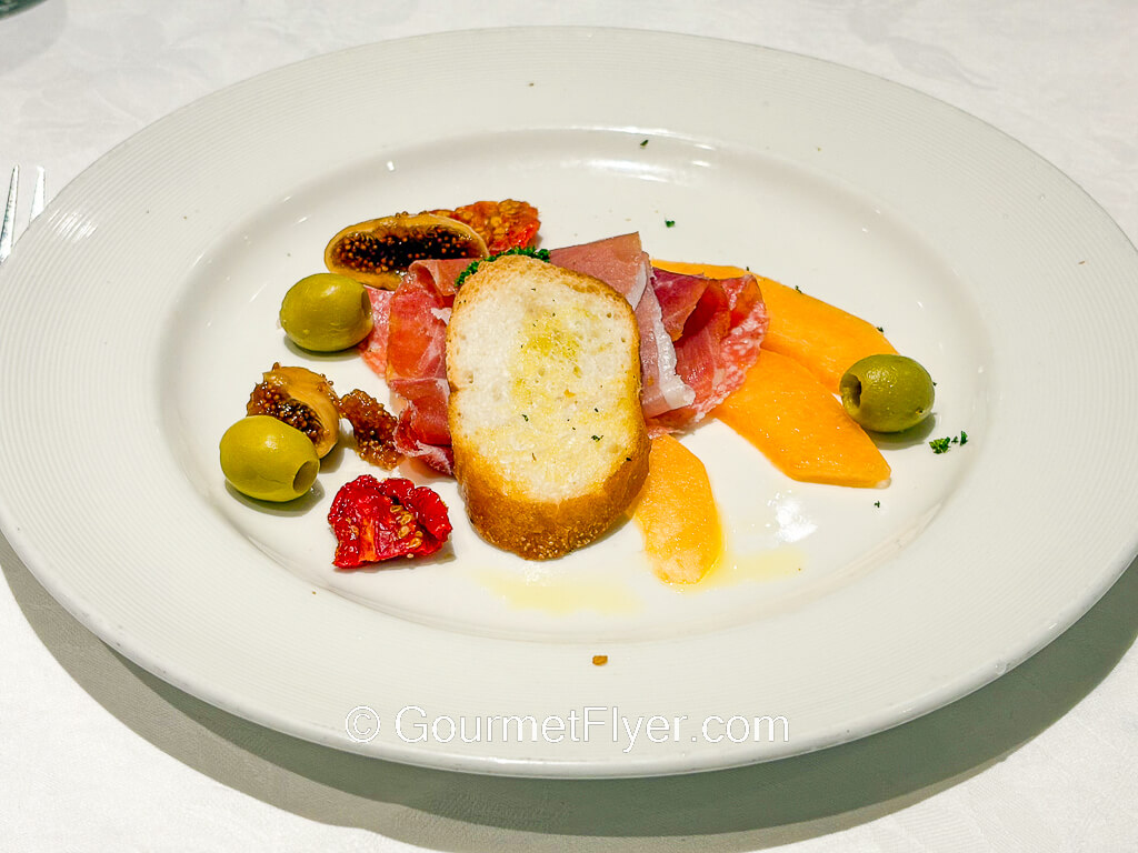 A beautifully arranged plate of sliced meats and fruits.