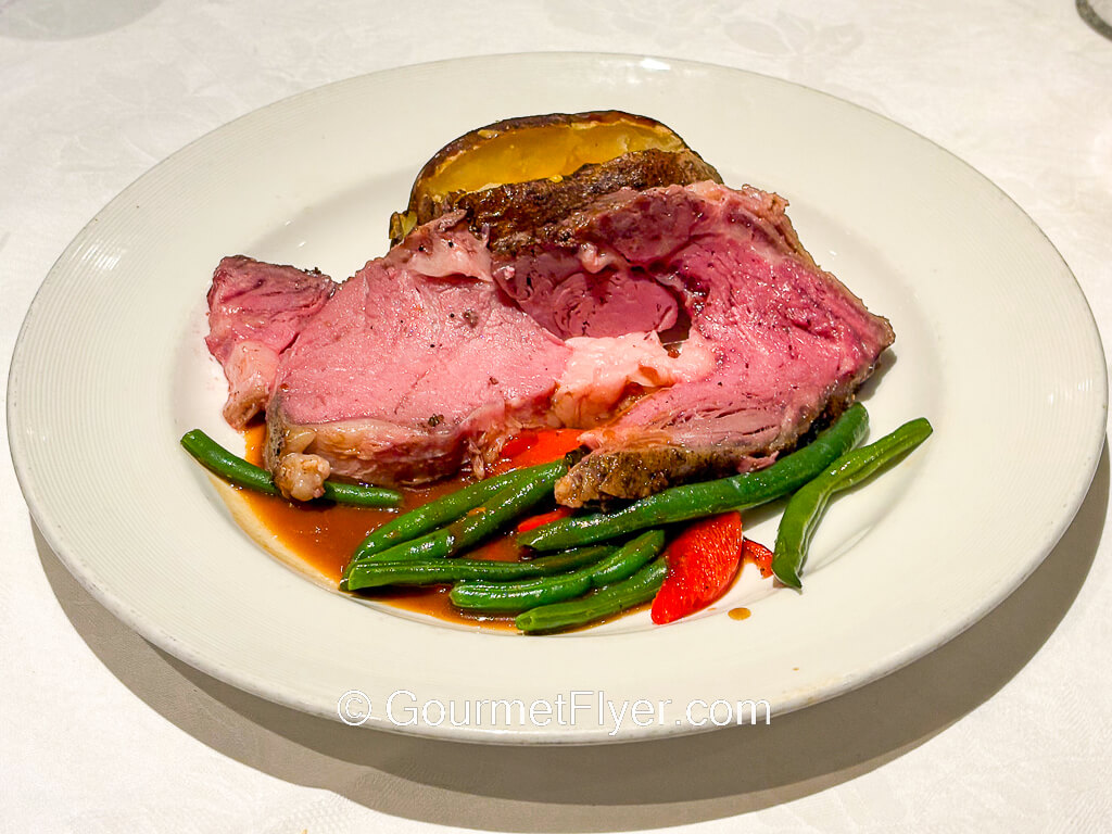 A pink slice of roast beef is accompanied by a baked potato.