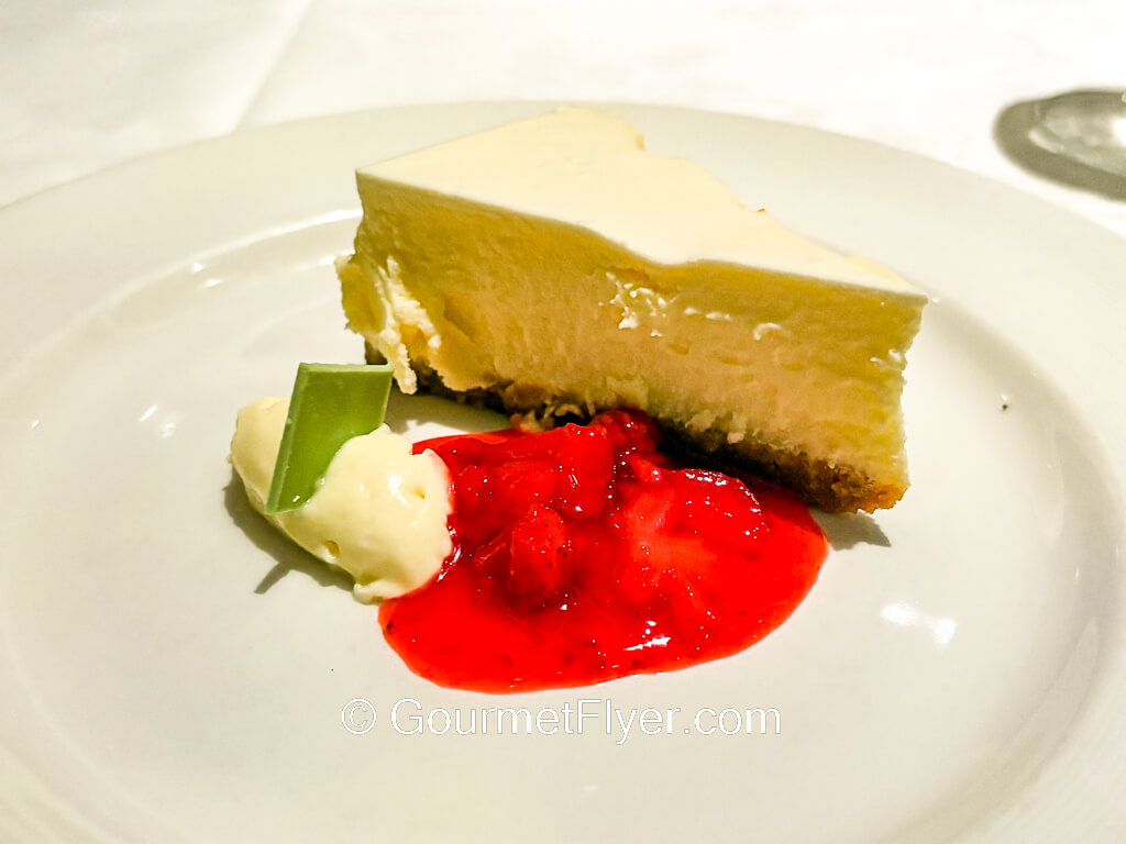 A slice of cake is served on a plate garnished with a red sauce.