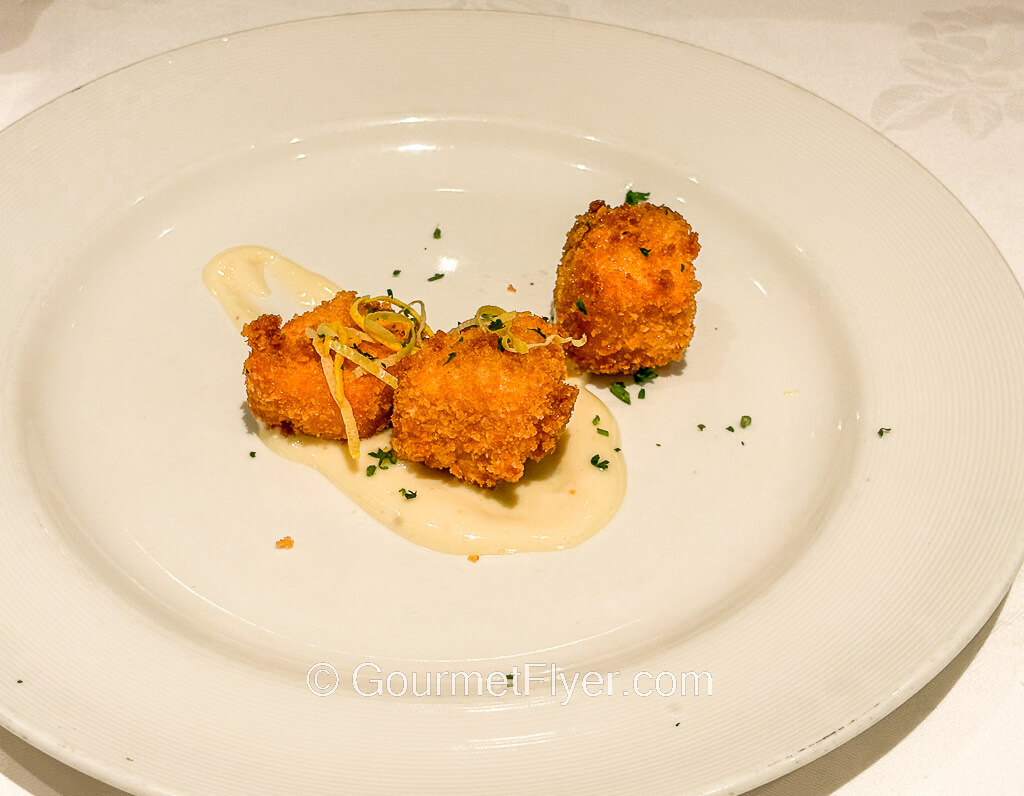 Three small pieces of fried fish is garnished with a yellowish cream sauce.