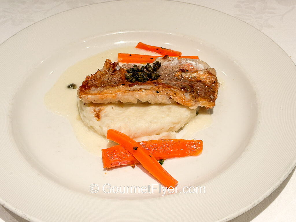A piece of fish is served skin side up over a bed of mashed potatoes.