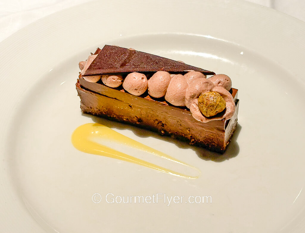 A piece of chocolate mousse like dessert is served on a plate and garnished with a yellow sauce. 