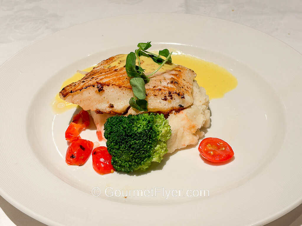 A piece of grilled fish is served with mashed potatoes and vegetables.