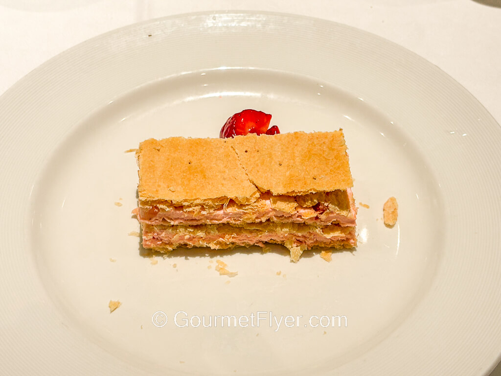 A crunchy and flaky dessert on a plate is garnished with cherries.