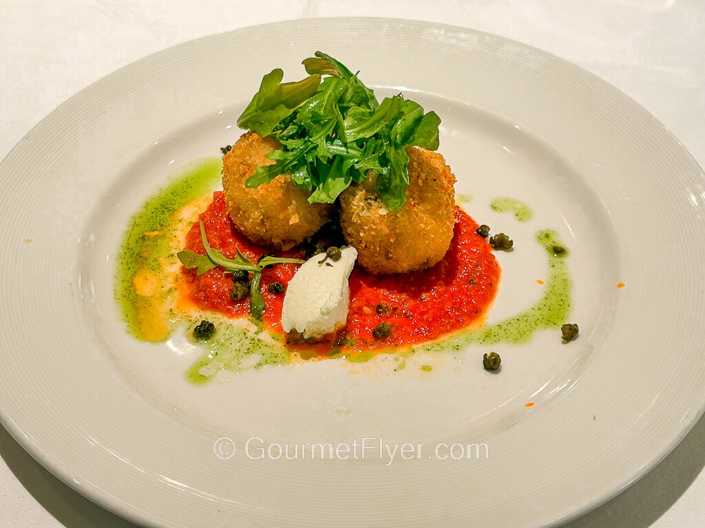 Two breaded fried dumplings are garnished with a red sauce.