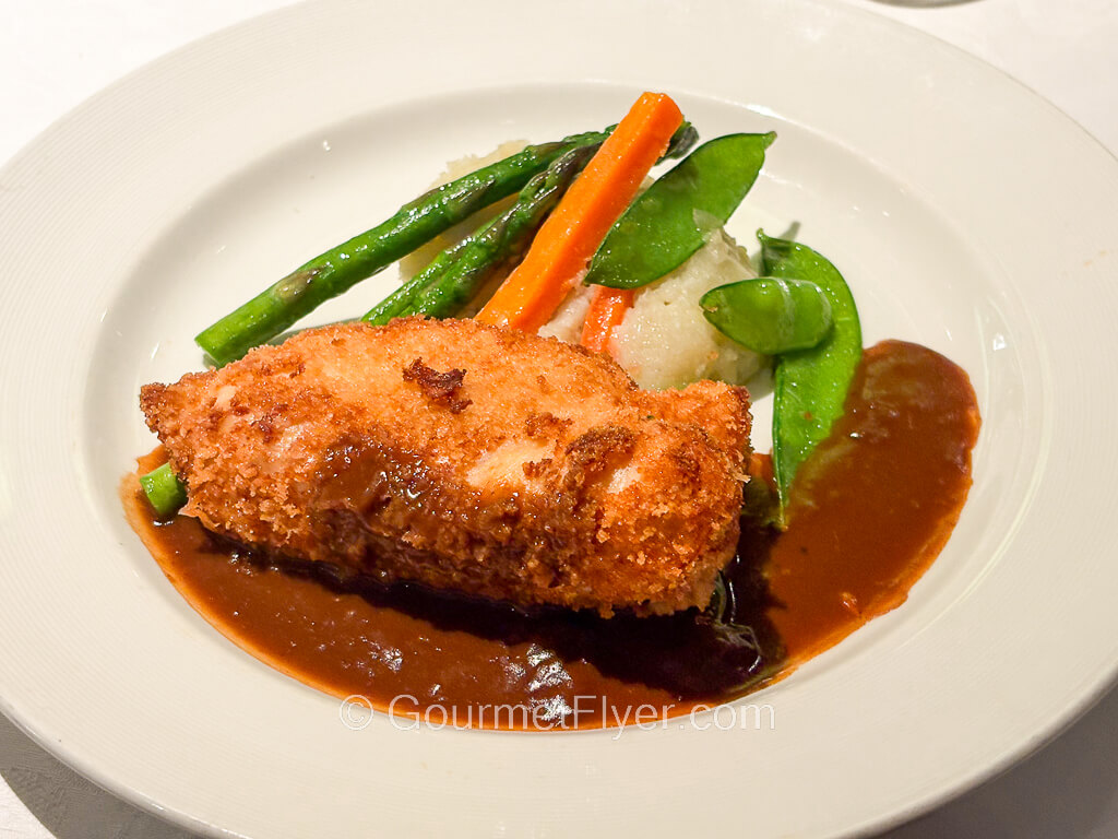 A piece of breaded meat fried to golden brown is served with brown gravy and vegetables.