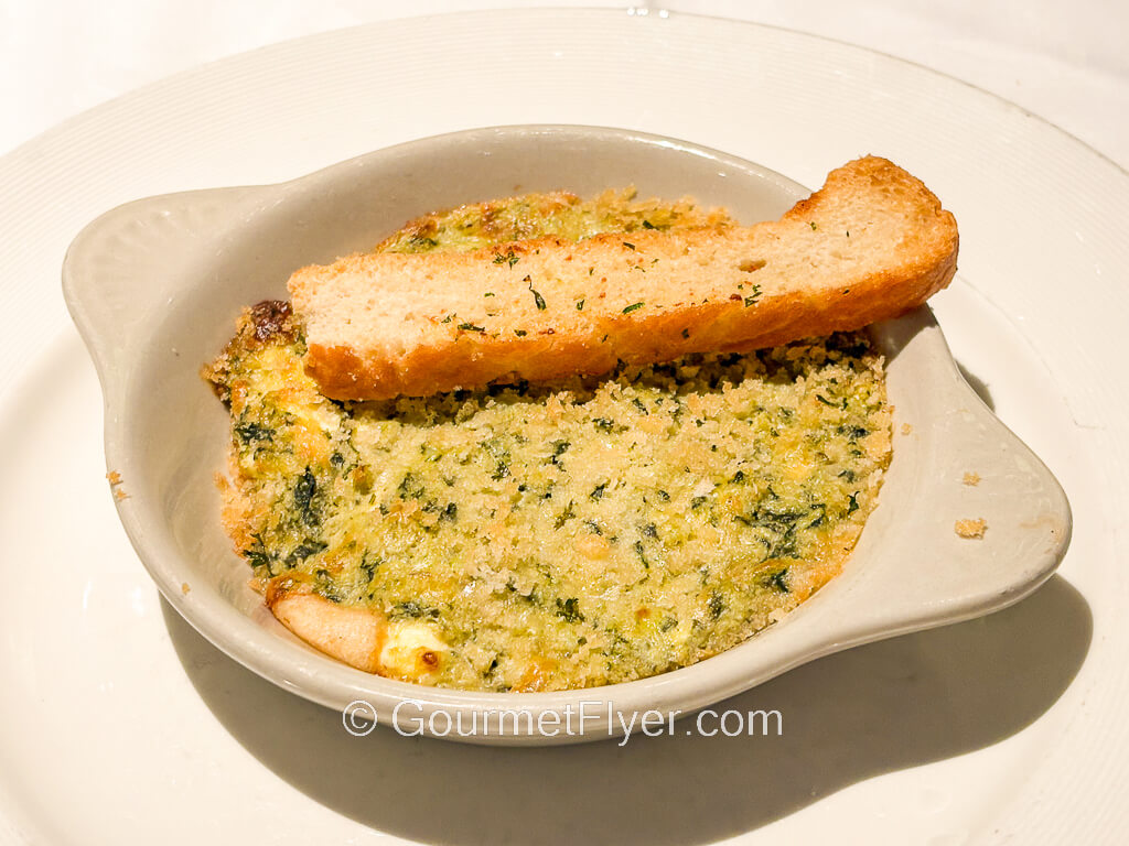 A shallow bowl contains a baked casserole topped with a baguette.