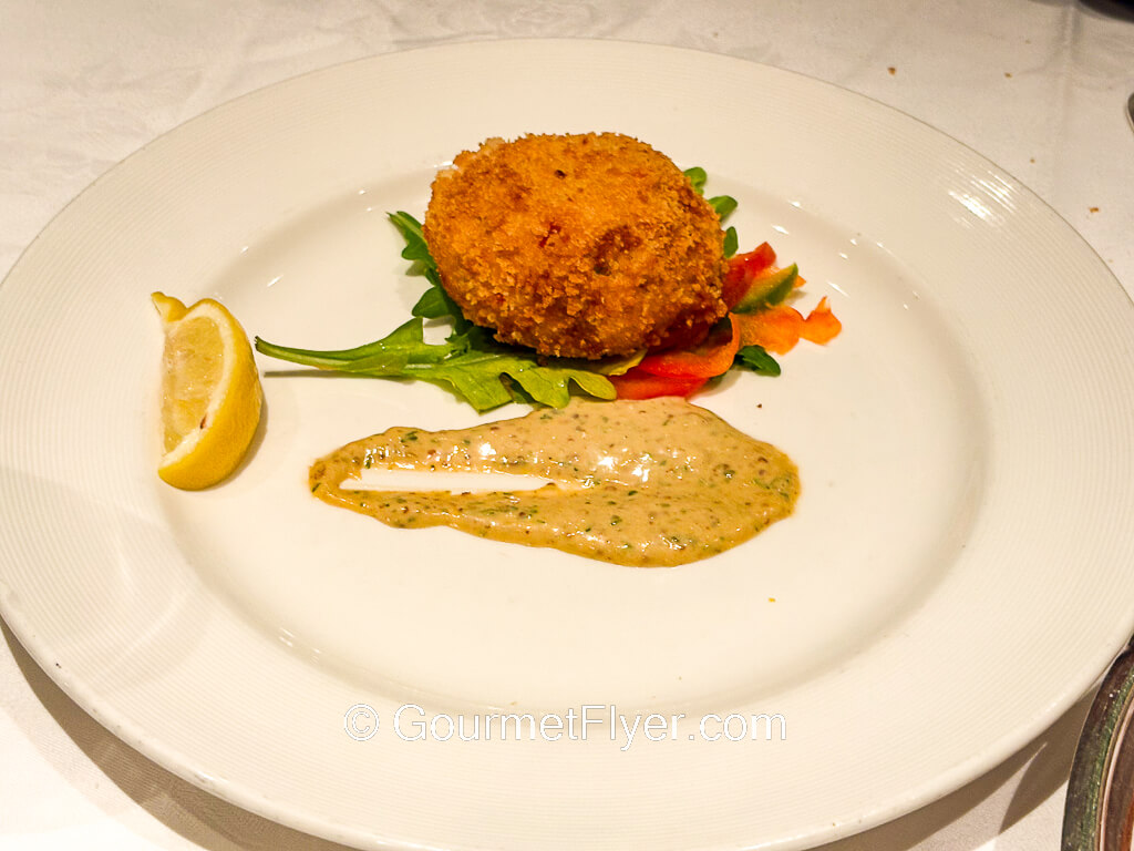 A deep-fried crab cake is garnished with a lemon wedge and mustard sauce.