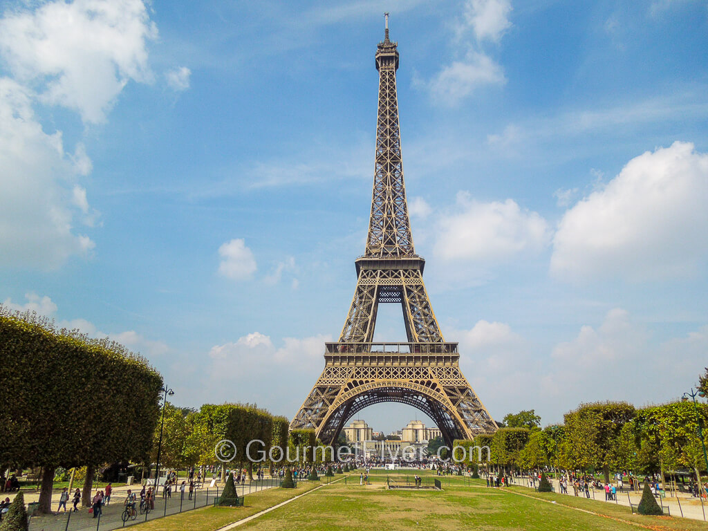 A 3-day in Paris itinerary features the Eiffel Tower standing behind a green landscape under a sunny blue sky.