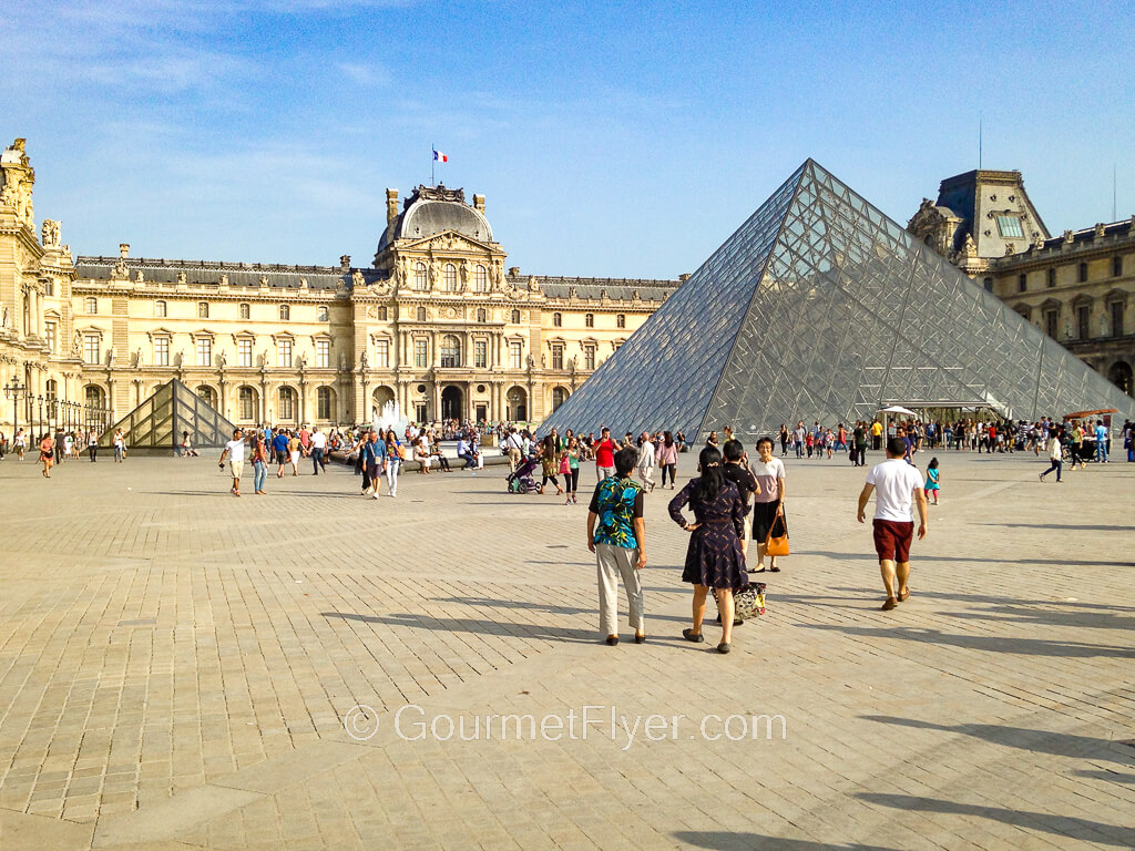 Tourists walk toward a glass pyramid that stands in front of the famous Louvre in Paris. 