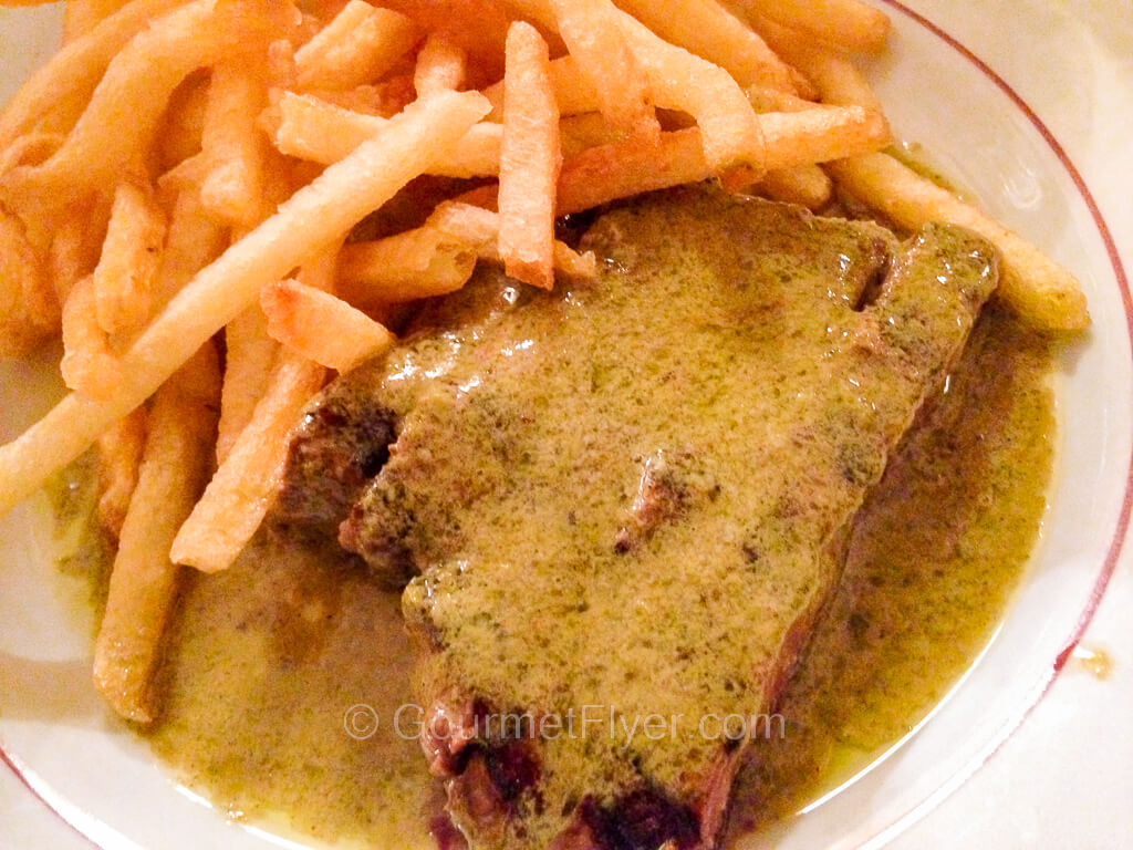 A steak is served in a pool of brownish green sauce and accompanied with French fries.