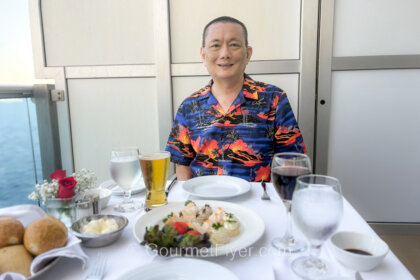 Princess Cruises Ultimate Balcony Dining Menu and Review features a blogger sitting in front of a table with white tablecloth and a full setting of tableware.