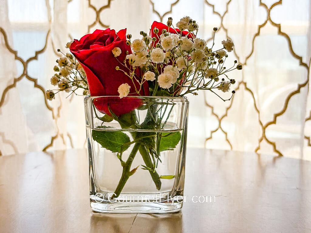 Roses and accompaniments are placed in a short and wide glass vase.