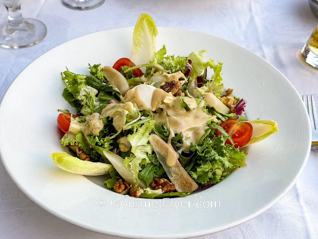 A green salad is topped with cherry tomatoes, nuts, and a creamy dressing.