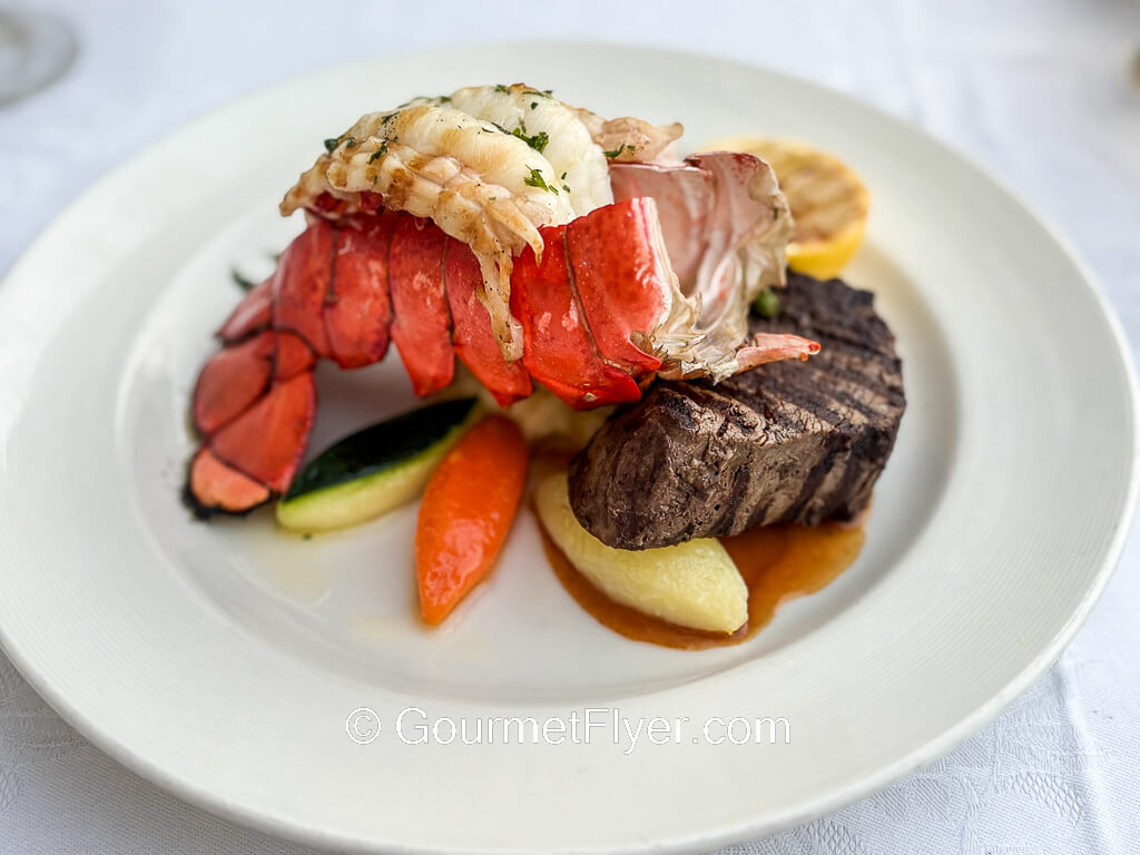 A grilled steak is accompanied by a lobster tail with its meat taken out of the shell and displayed on top of it.