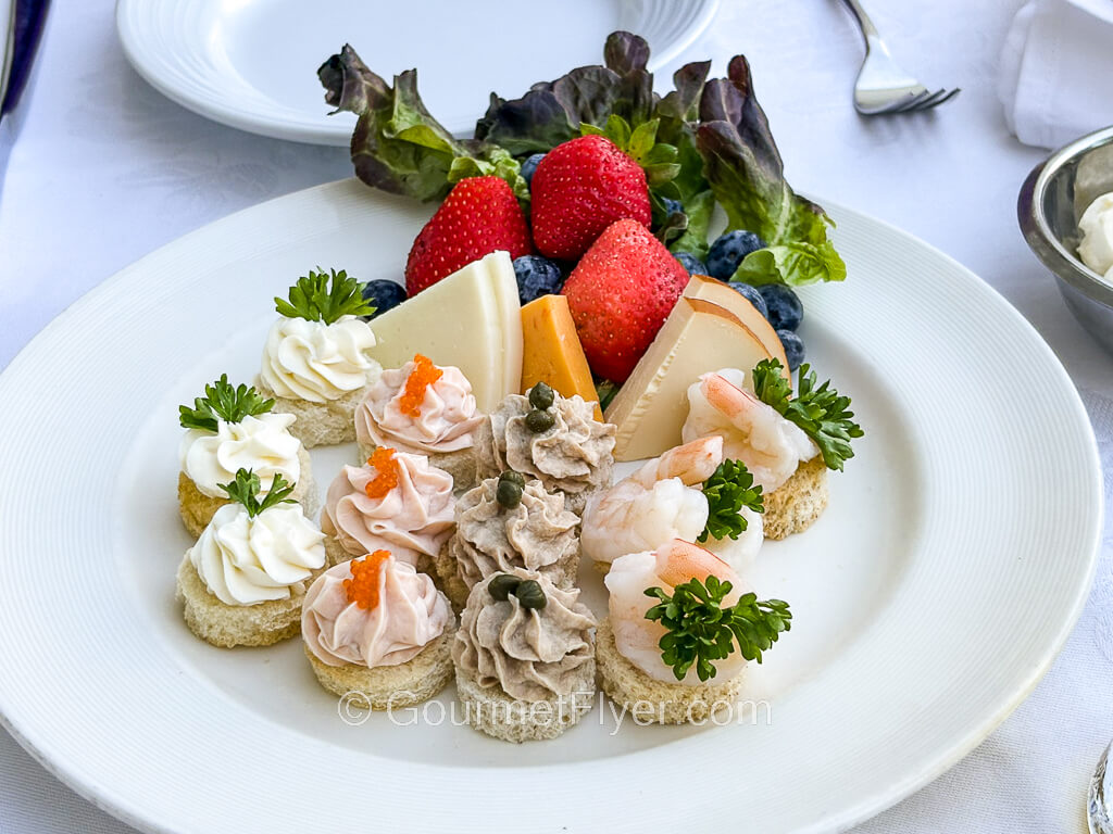 Four rows of canapes of different flavors are arranged on a plate that is garnished with greens and strawberries.