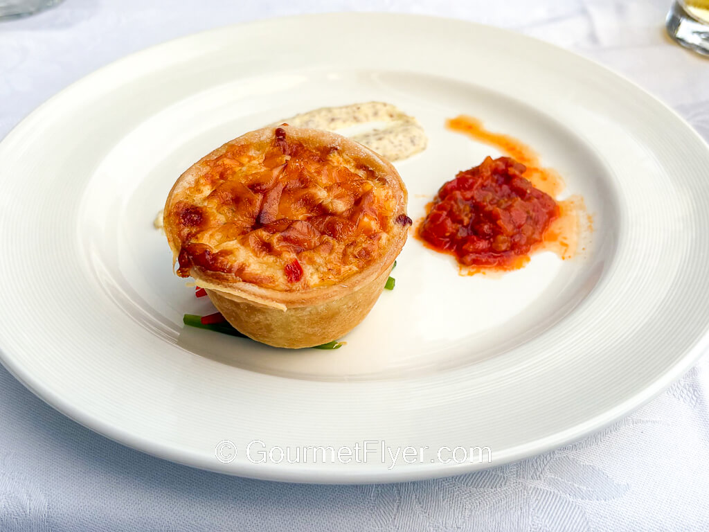A quiche like pastry is served on a plate garnished with a red sauce and a cream sauce.