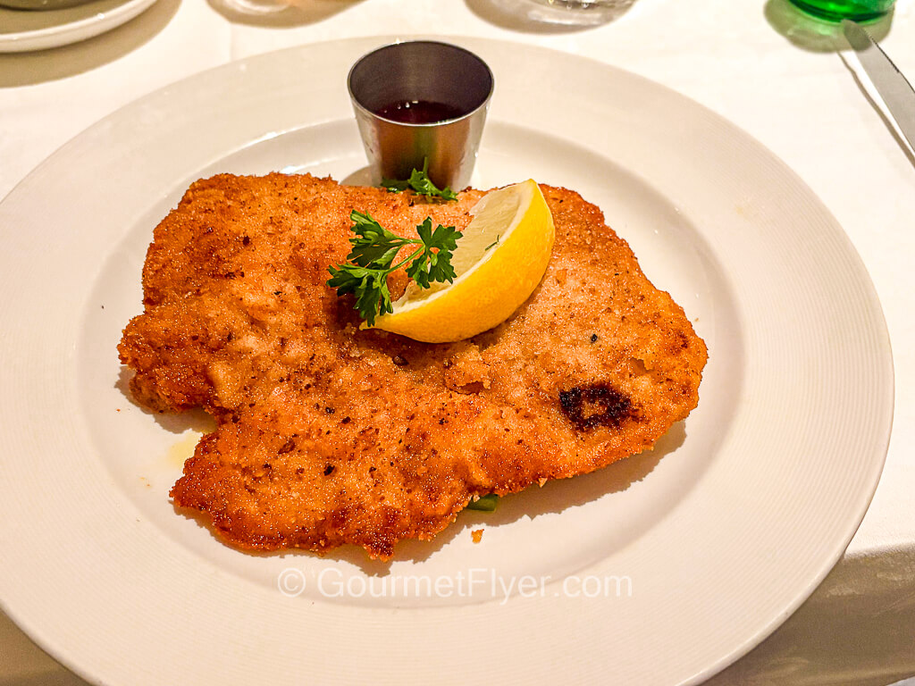 A slab of breaded fired meat is topped with a lemon wedge.