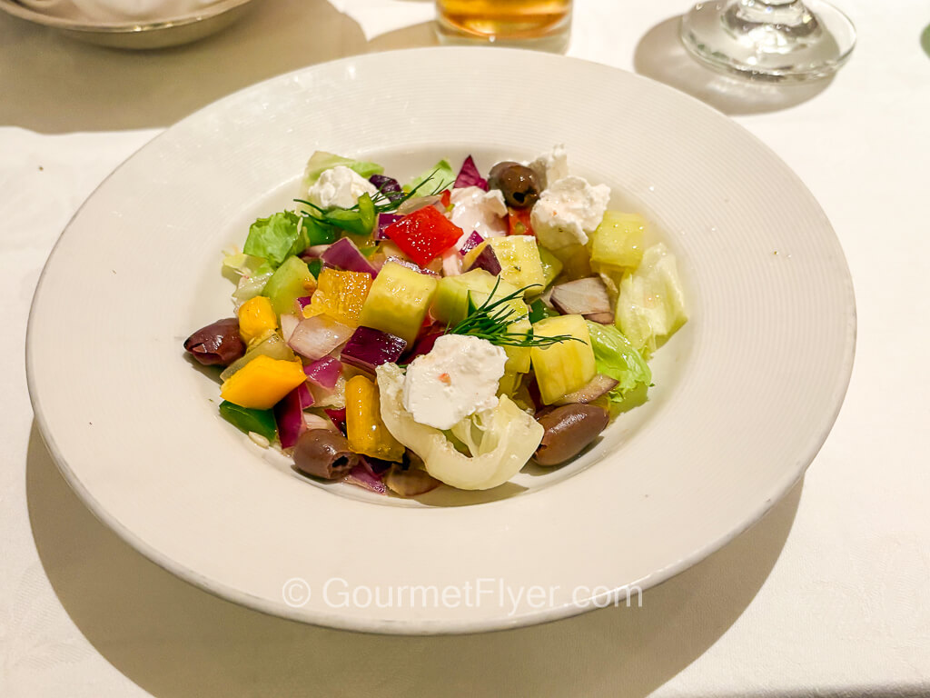 A deep-dish bowl contains a salad of many different cut and cubed vegetables.