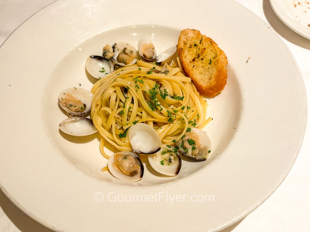A plate of thin pasta with clams is accompanied by a slice of garlic bread.