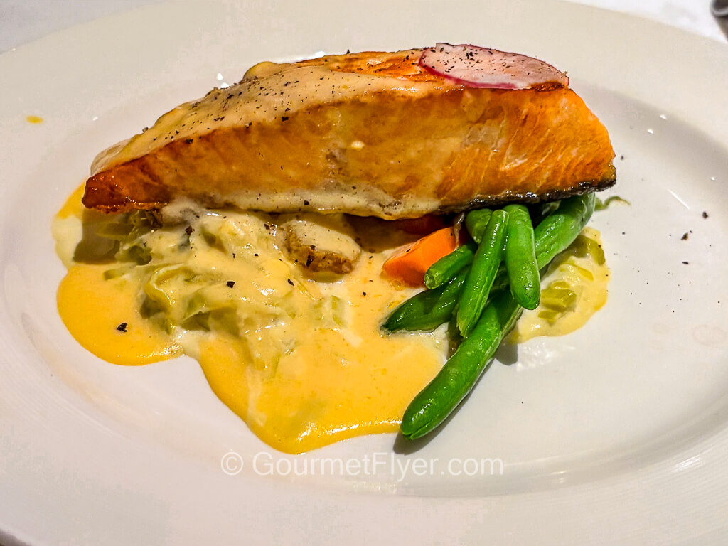 A thick piece of grilled fish is served on a plate with a yellowish creamy cheese sauce.