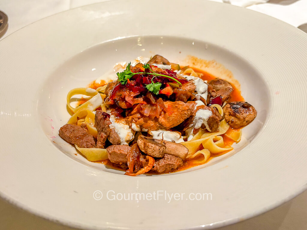 Wide noodle-like pasta is tossed with meat in a red sauce.