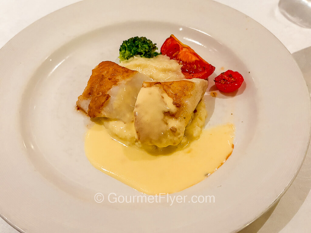 A piece of grilled fish is served with a creamy and cheesy yellow sauce.