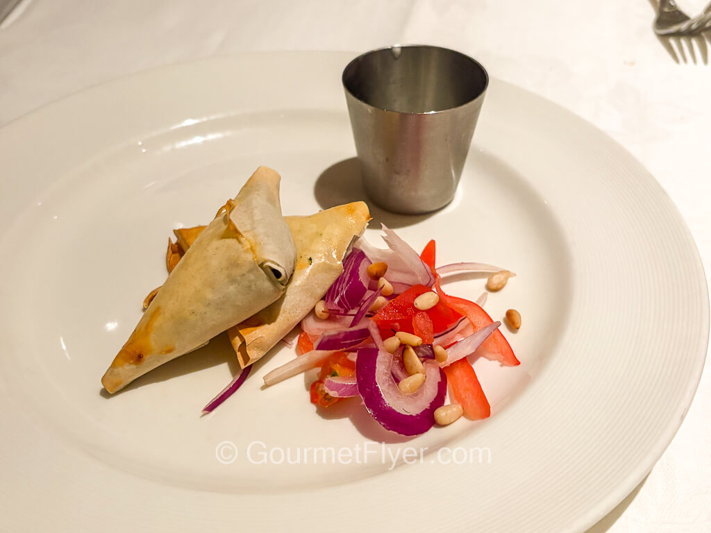 Two triangular fried puff pastries are accompanied by a blend of onions and peppers.