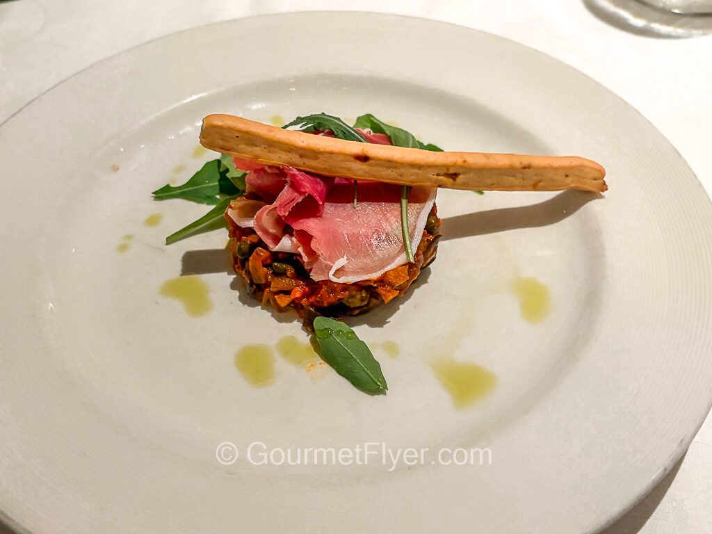 A thin slice of deli meat sits atop a bed of grains, topped with a breadstick.