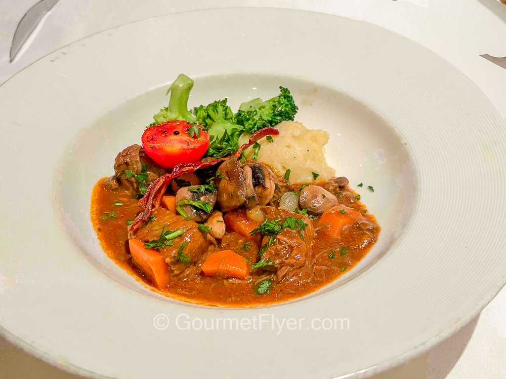 A beef stew dish is garnished with broccoli, carrots, and tomatoes.