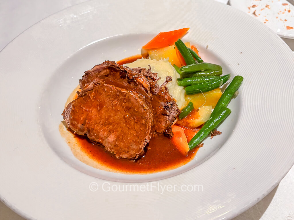 Three slices of meat are served with brown gravy and accompanied with mixed vegetables.