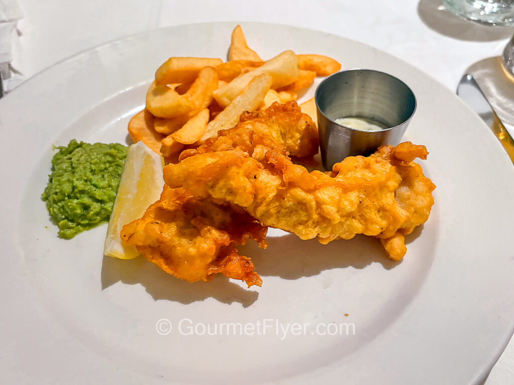 A plate of fish and chips is garnished with mashed peas and a lemon wedge.