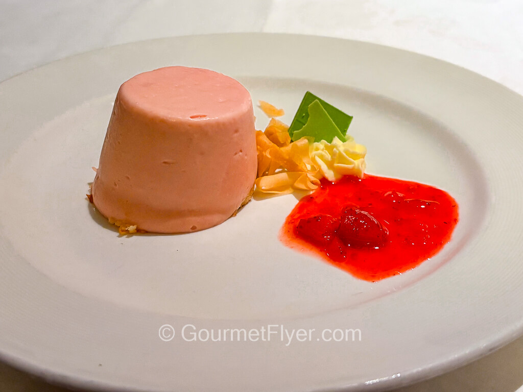 A molded pink mousse is served with red strawberry sauce